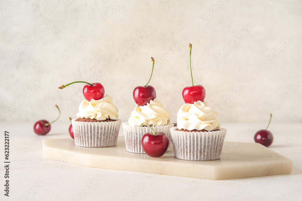 Board with tasty cherry cupcakes on light background