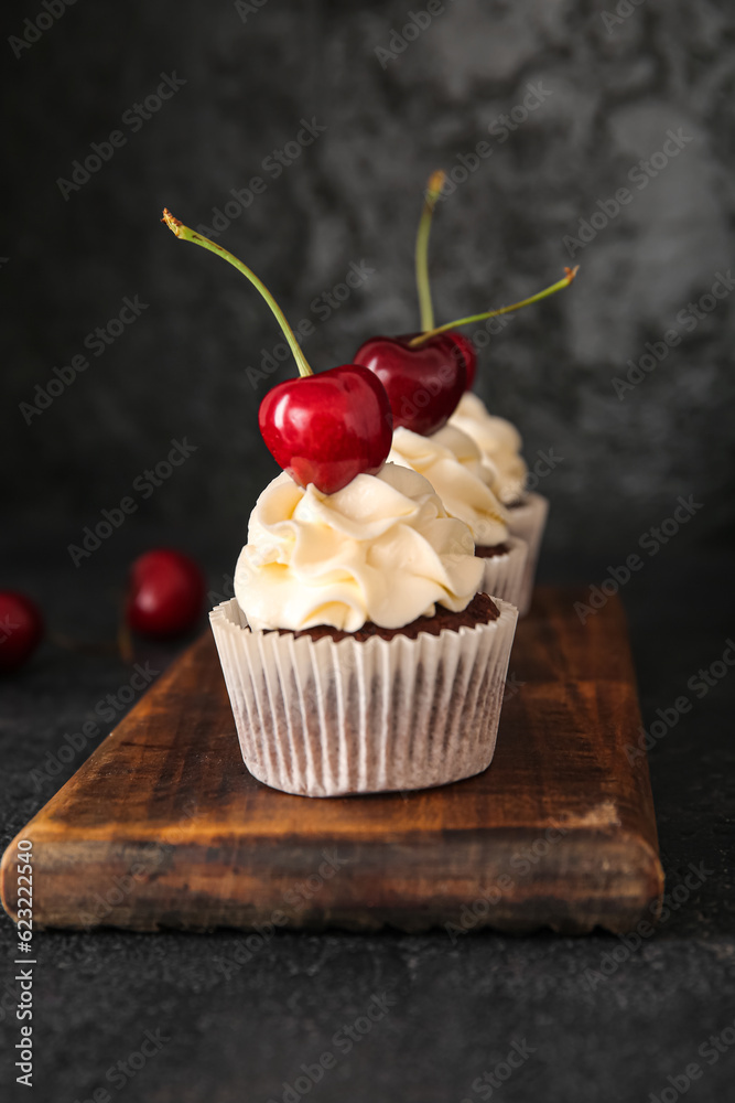 Wooden board with tasty cherry cupcakes on black background