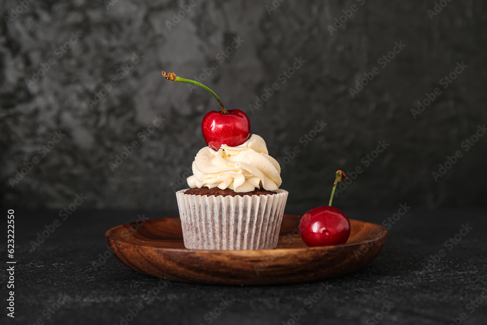 Plate with tasty cherry cupcake on black background