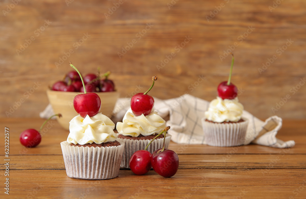 Tasty cherry cupcakes on wooden background