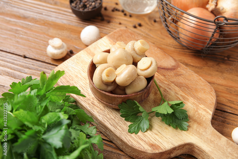 Bowl with canned mushrooms on wooden background