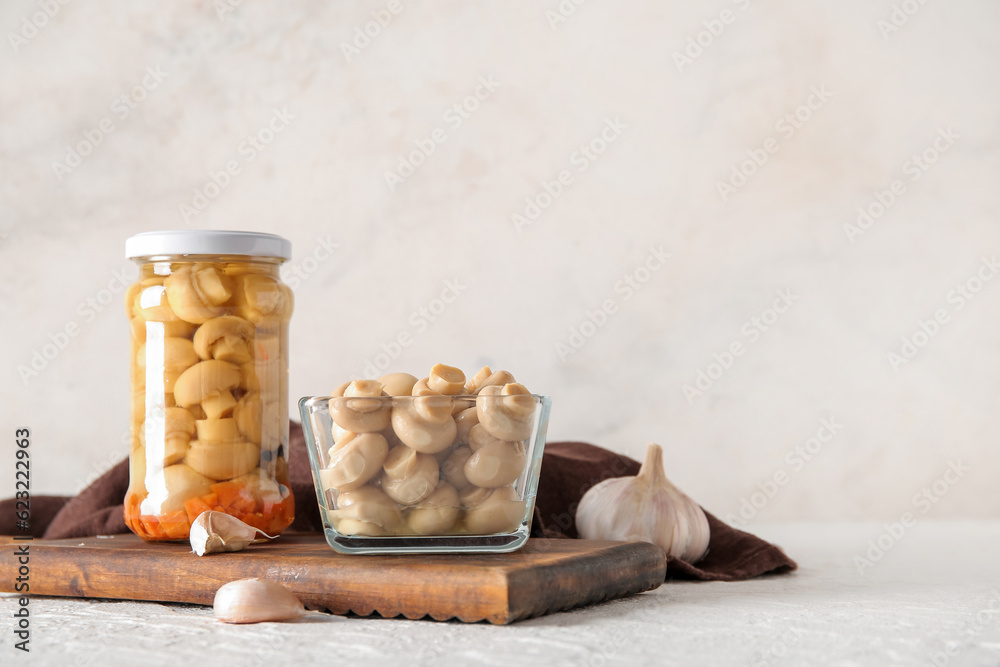 Jar and bowl with canned mushrooms on light background