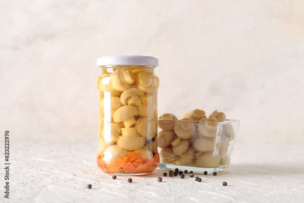 Jar and bowl with canned mushrooms on light background