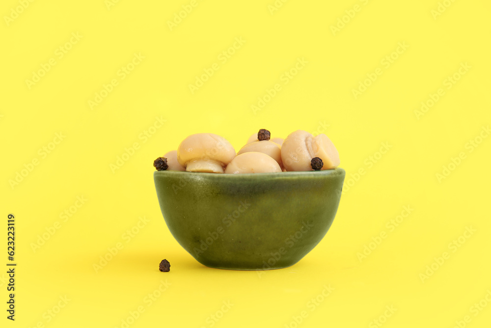 Bowl with canned mushrooms on yellow background