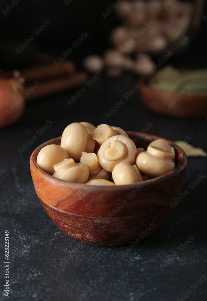 Bowl with canned mushrooms on black background