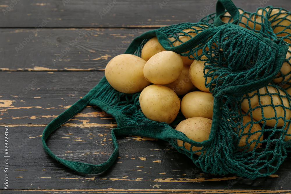 String bag with raw potatoes on black wooden background