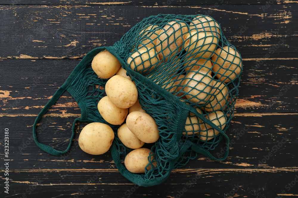 String bag with raw potatoes on black wooden background