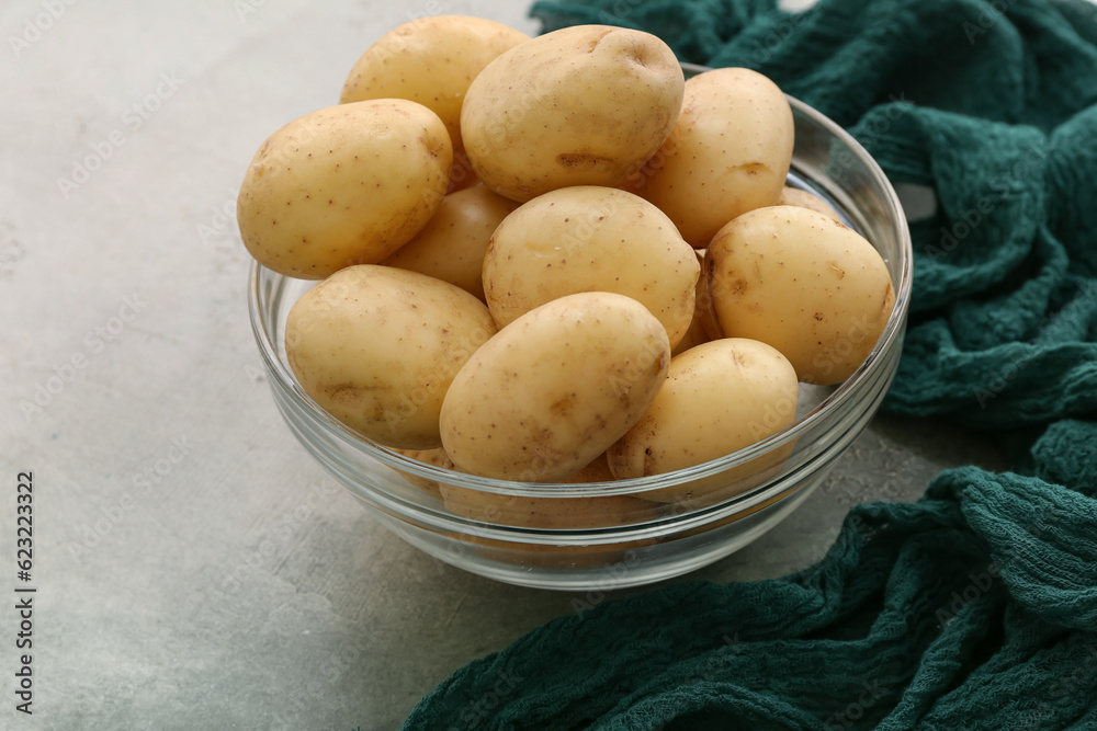 Glass bowl with raw potatoes on white background