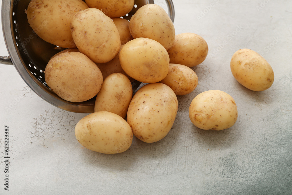 Colander with raw potatoes on white background