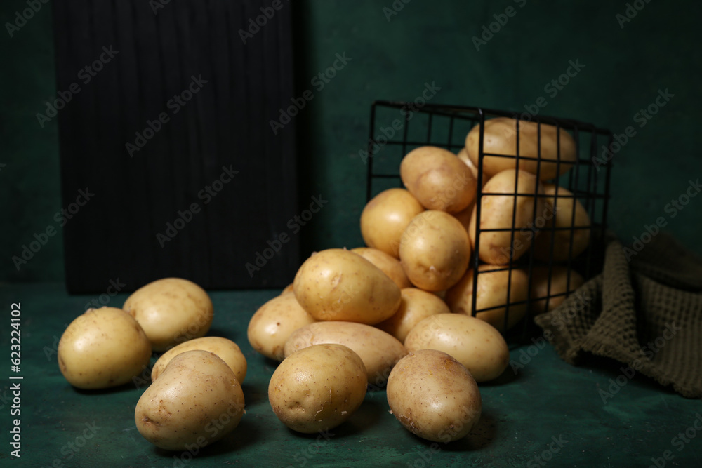 Basket with raw potatoes on green background