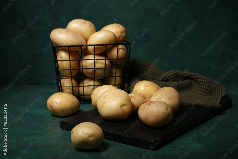 Board and basket with raw potatoes on green background