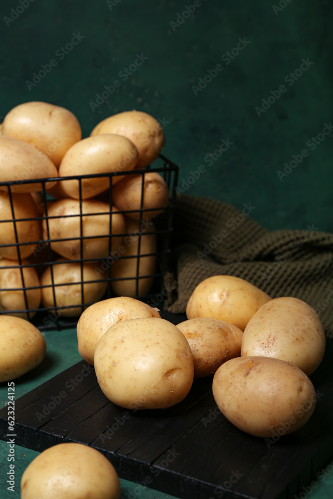 Board and basket with raw potatoes on green background