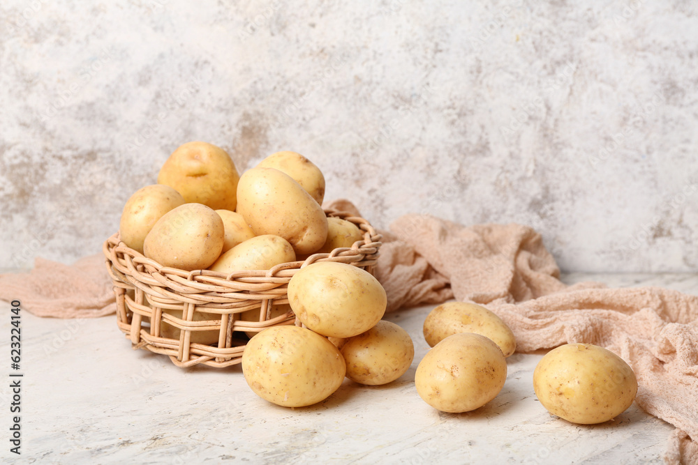 Wicker bowl with raw potatoes on white table