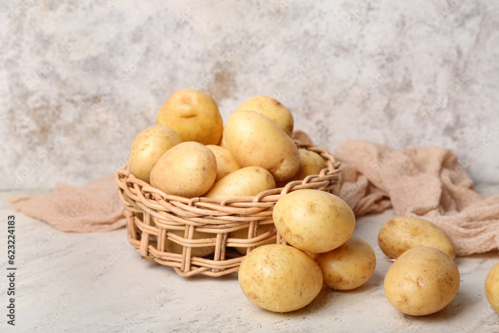 Wicker bowl with raw potatoes on white table