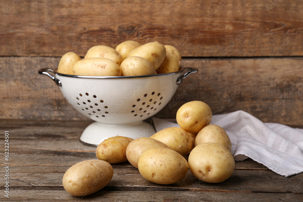 Colander with raw potatoes on wooden background