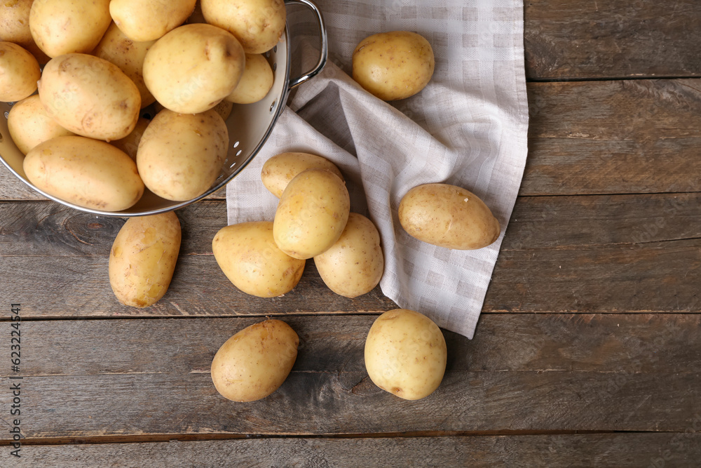 Colander with raw potatoes on wooden background