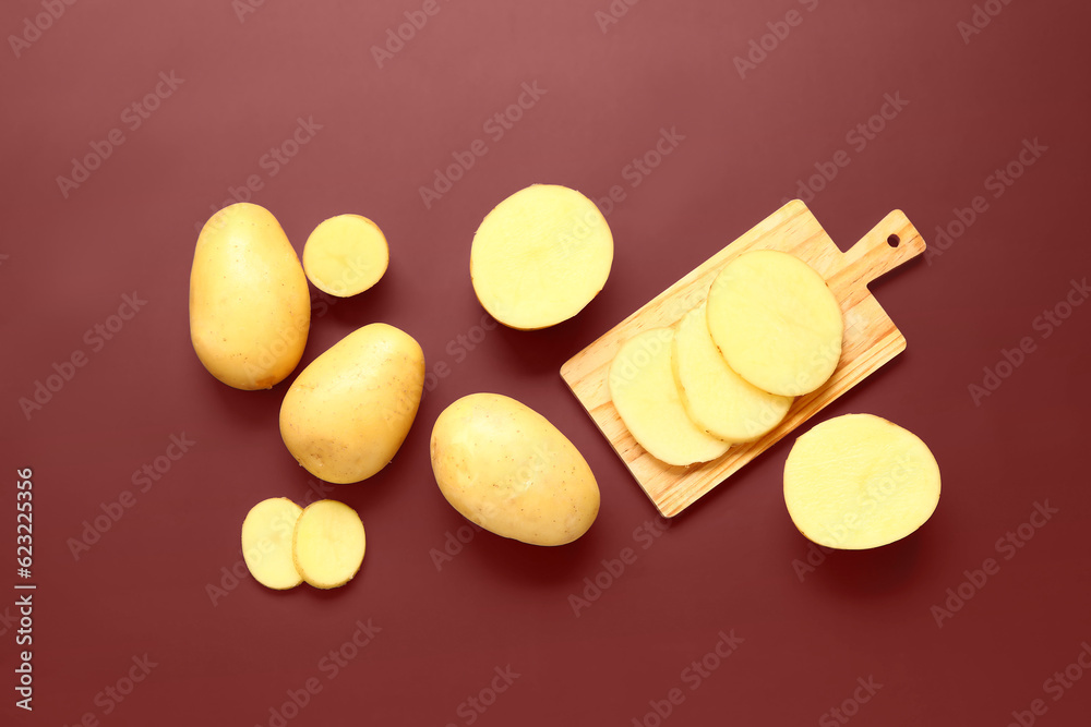 Wooden board with raw potatoes on brown background