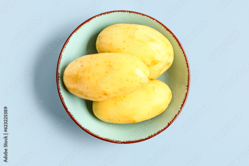 Bowl with raw potatoes on blue background