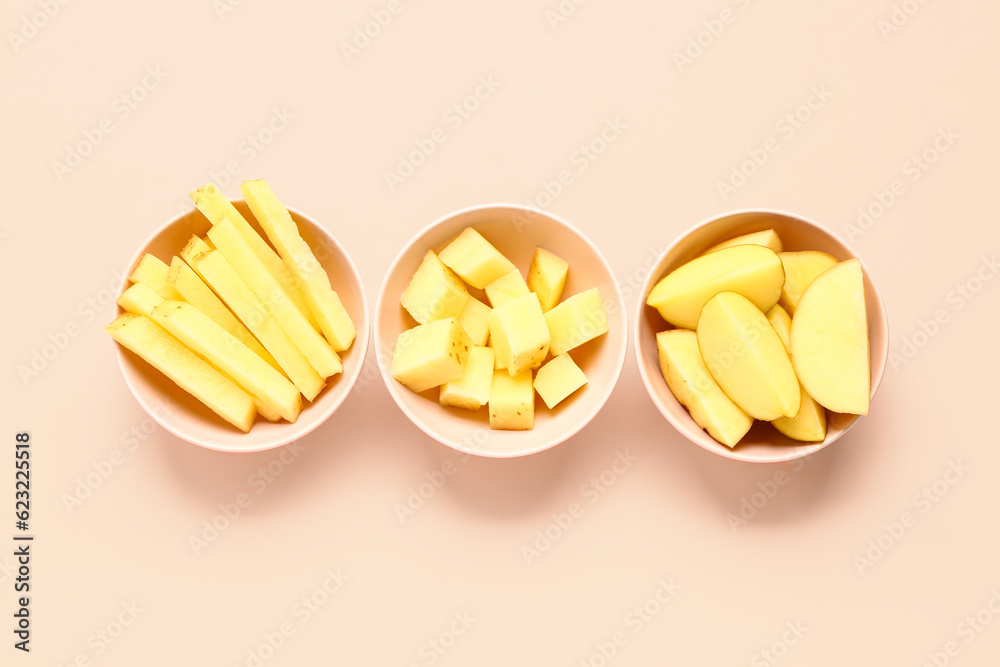 Bowls with pieces of raw potato on pink background