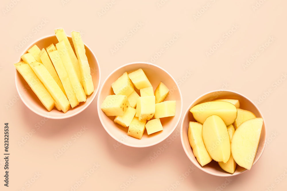 Bowls with pieces of raw potato on pink background