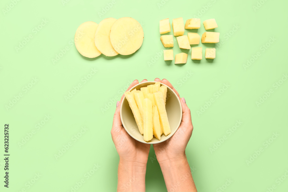 Woman holding bowl with pieces of raw potato on green background