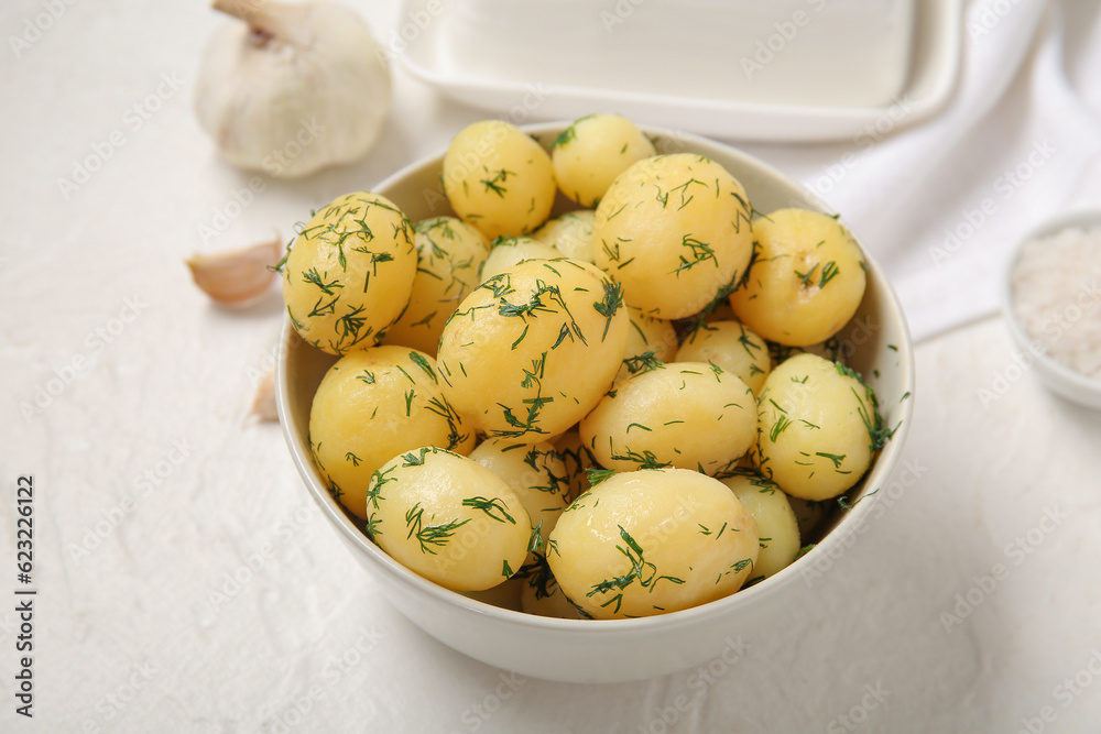 Bowl with boiled baby potatoes on light background