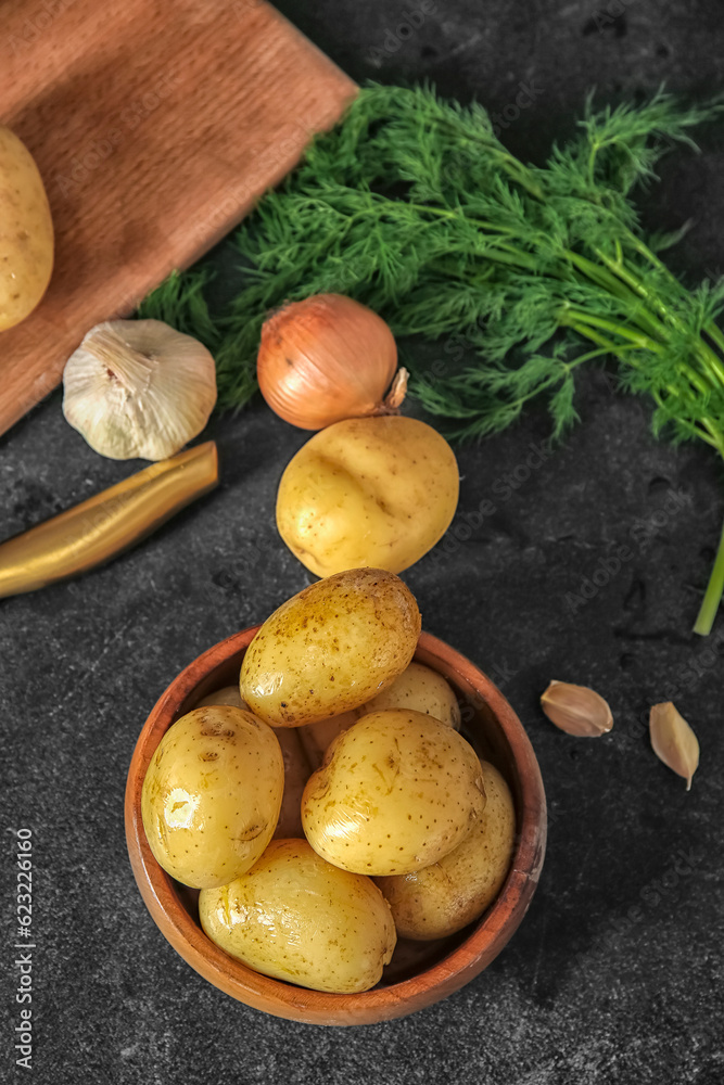 Bowl with raw potatoes on black background