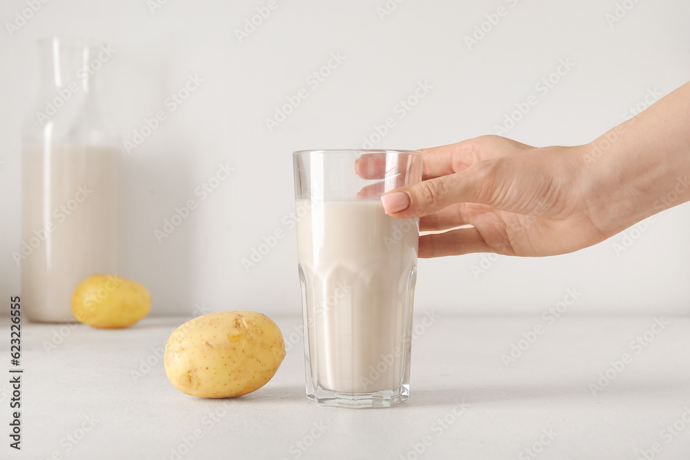 Woman holding glass of tasty potato milk on light background