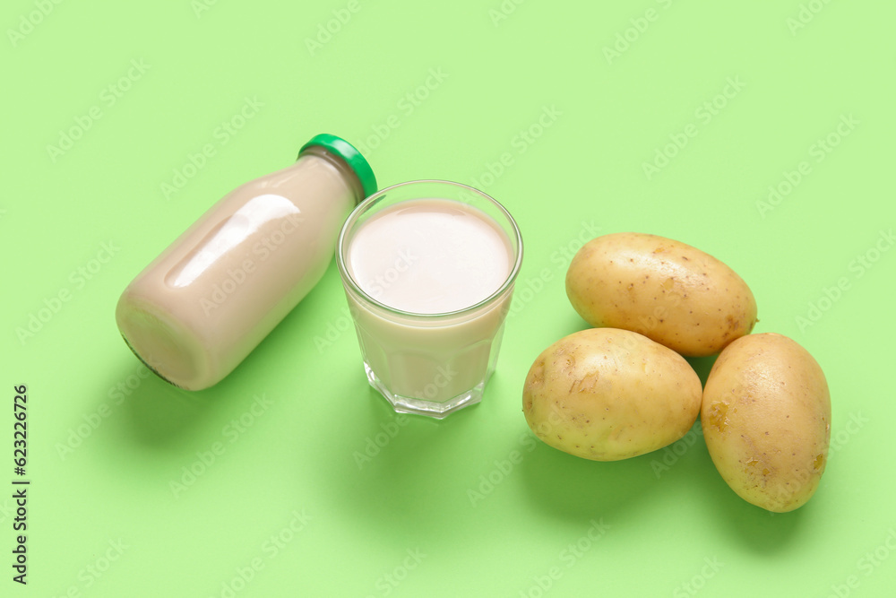 Bottle and glass of tasty potato milk with fresh vegetables on green background