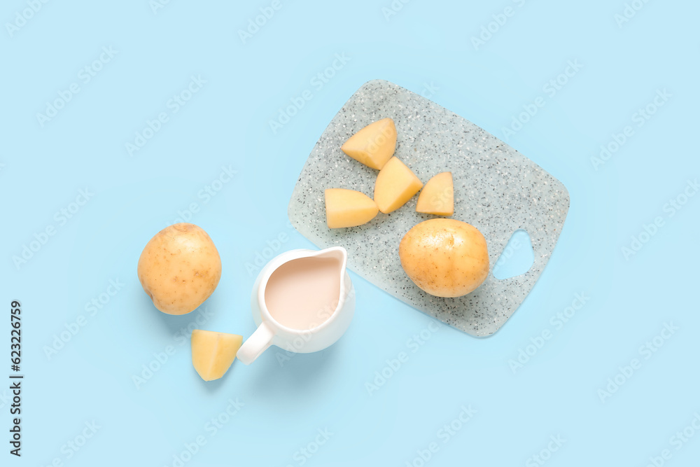 Jug of tasty potato milk and fresh vegetables on blue background