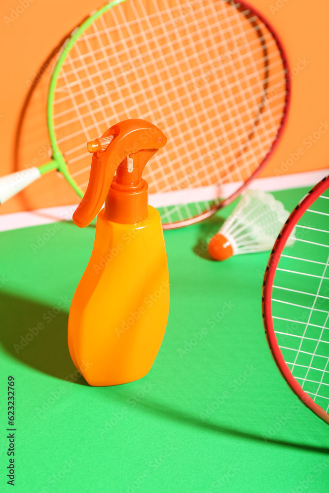 Bottle of sunscreen cream, badminton rackets and shuttlecock on color background