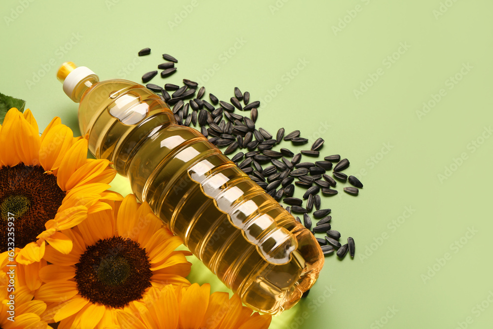 Sunflowers, seeds and bottle of oil on green background