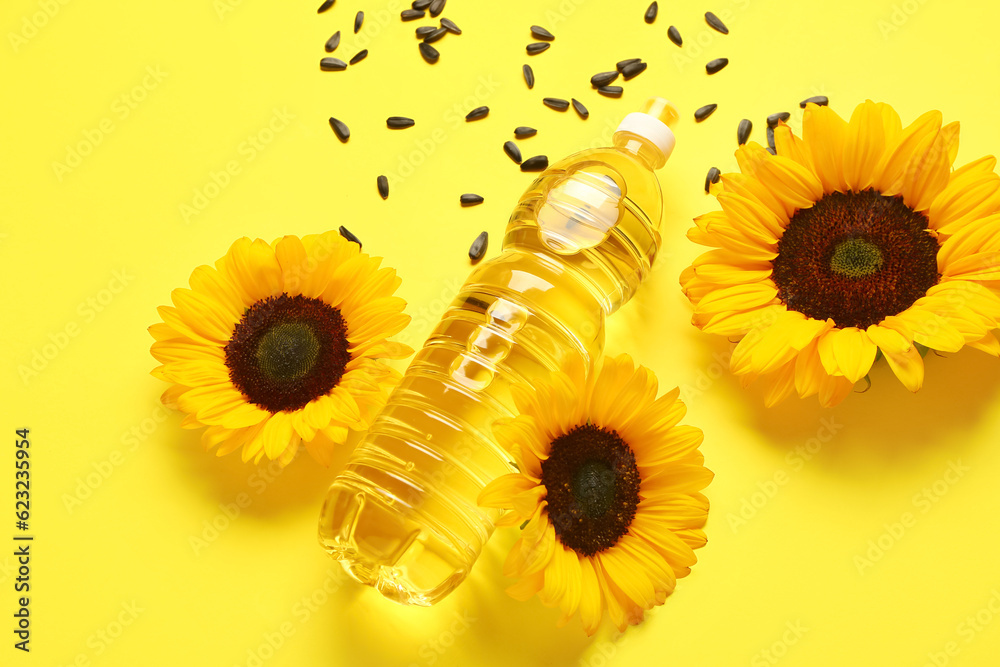 Sunflowers, seeds and bottle of oil on yellow background