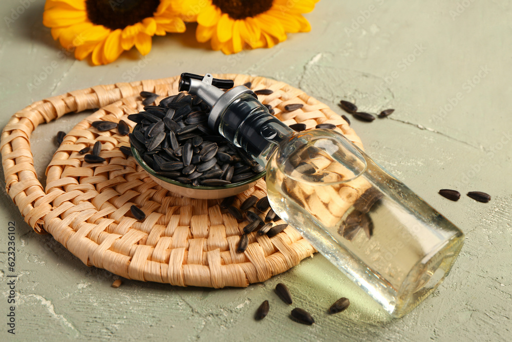 Bottle of sunflower oil and seeds on green background