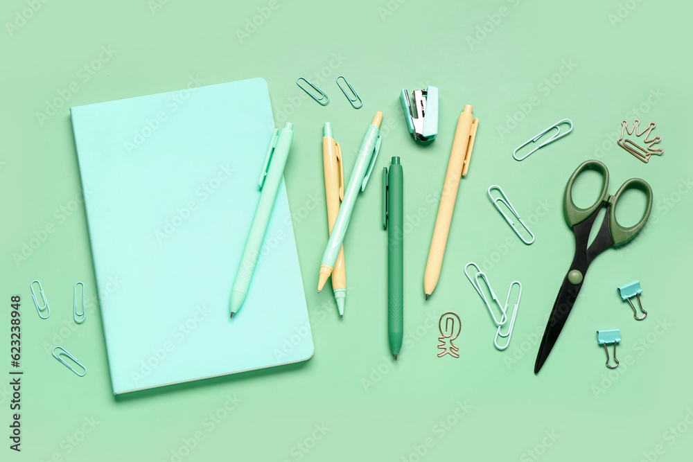 Notebook with different school stationery on green background