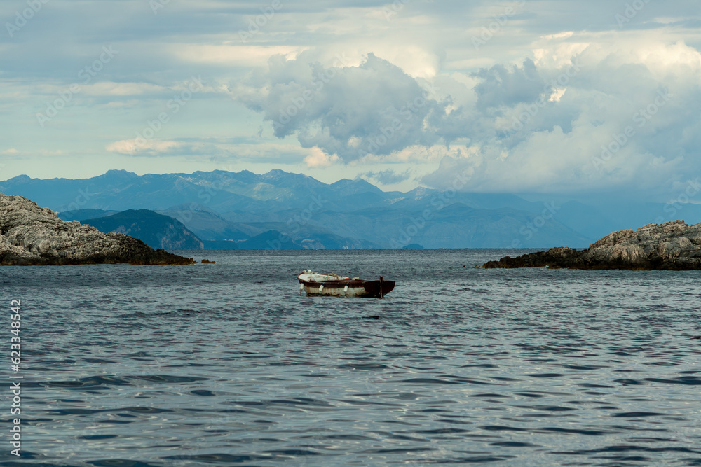 A lonely old wooden fishing boat in a sea bay with cloudy sky and islands background. Croatia, Europ