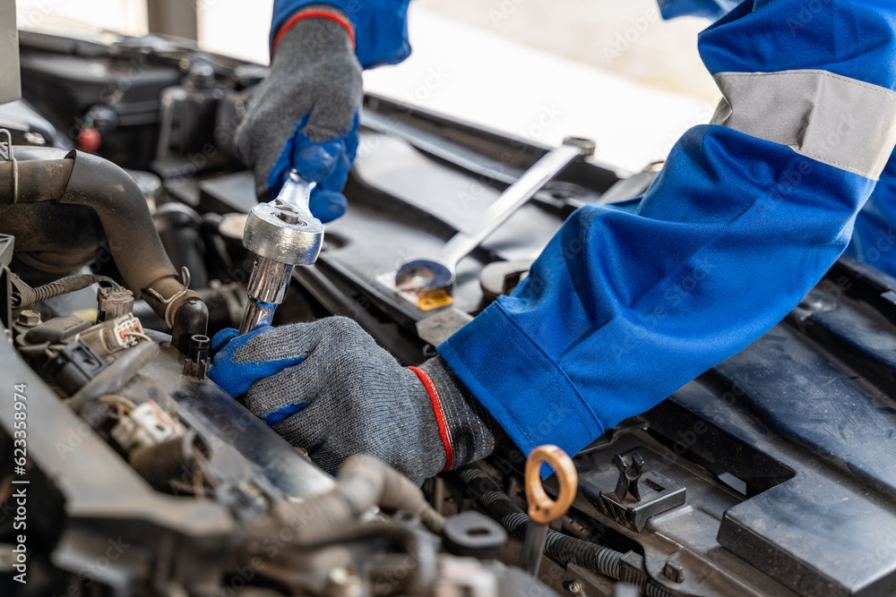 Close up hands of a male car mechanic using retchet wrench while working on cars engine