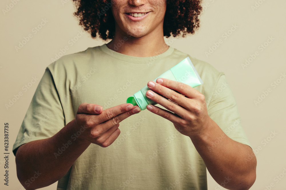 Happy young man applying a facial mask on his fingers, starting his skincare routine