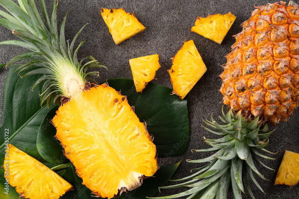 Fresh cut pineapple with tropical leaves on dark gray table background.