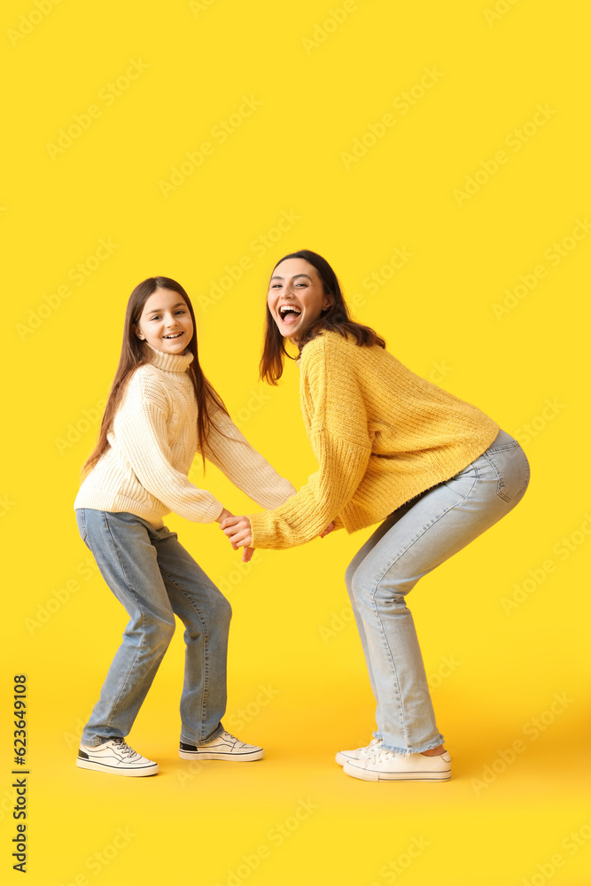 Little girl and her mother in knitted sweaters dancing on yellow background