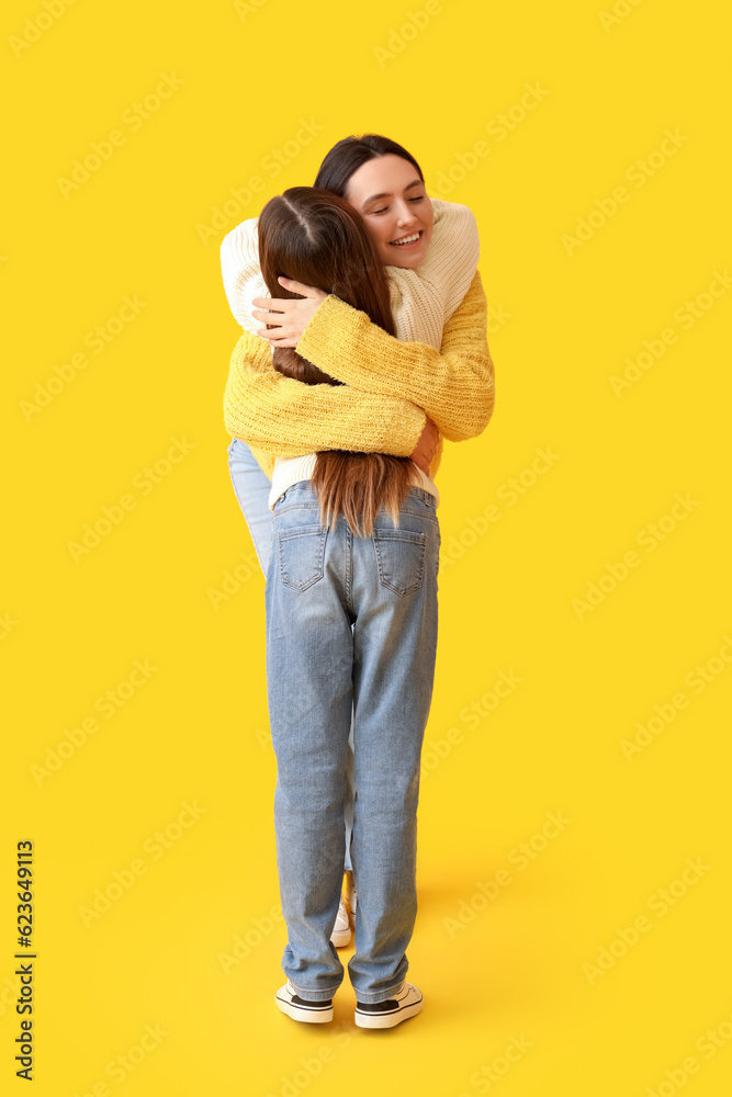 Little girl and her mother in knitted sweaters hugging on yellow background