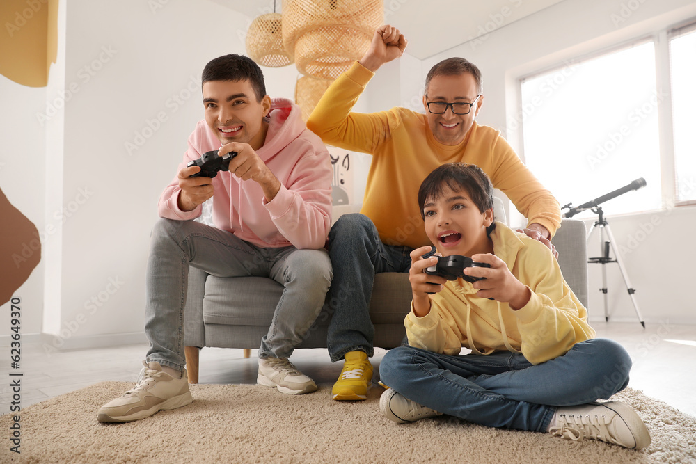 Happy little boy with his dad and grandfather playing video game at home