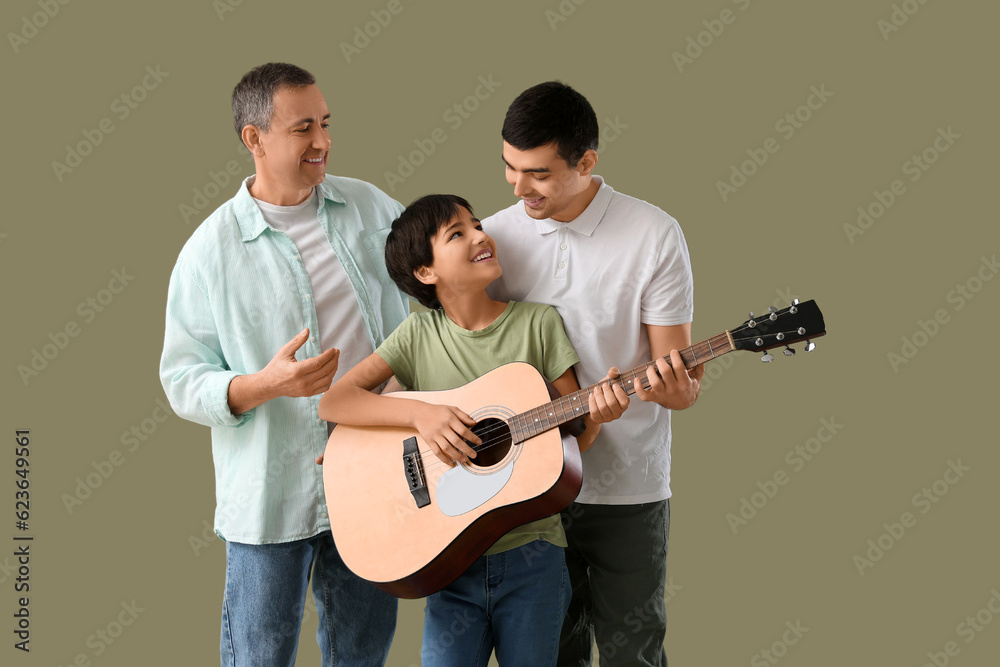 Happy little boy with his dad and grandfather playing guitar on green background