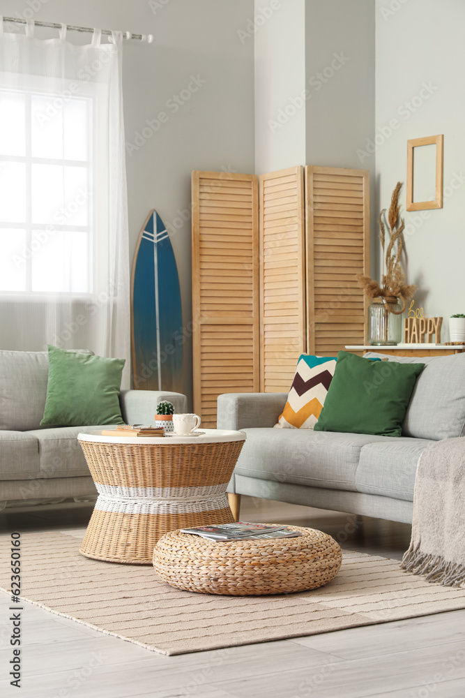 Interior of light living room with surfboard, table and sofas