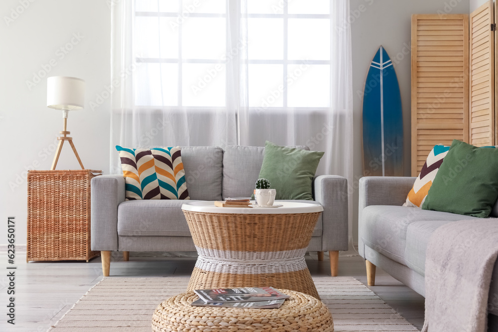 Interior of light living room with surfboard, table and sofas