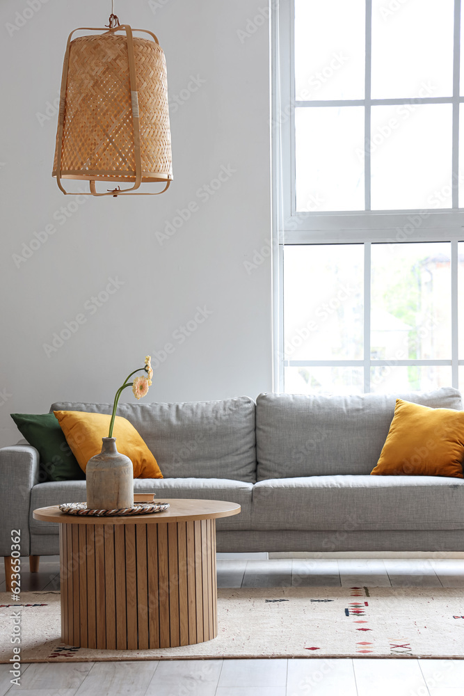 Interior of light living room with grey sofa, wooden coffee table and big window