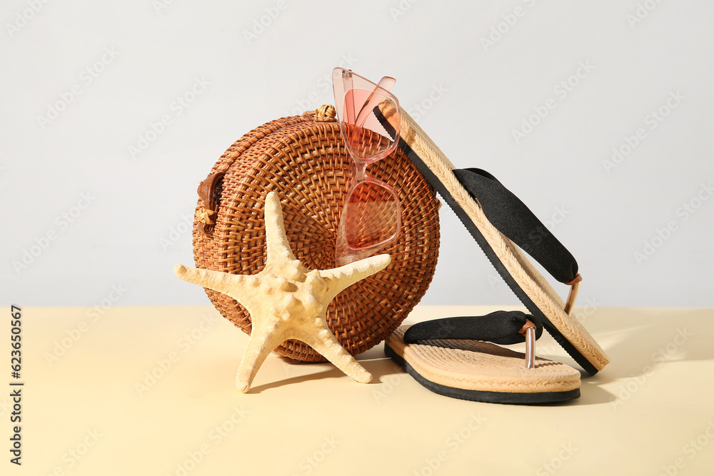 Stylish sunglasses with bag and flip flops on light table