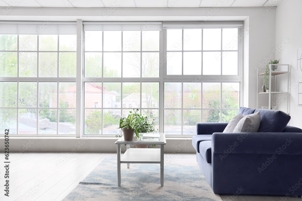 Interior of light living room with cozy blue sofa and modern laptop on table near big window