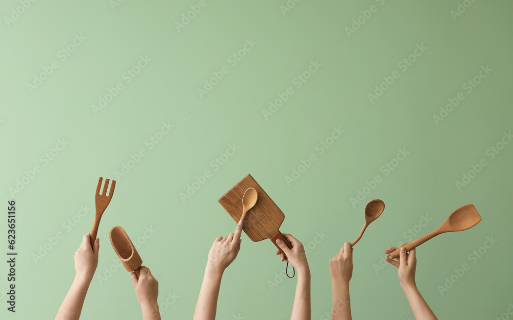 Women with wooden kitchen utensils on green background