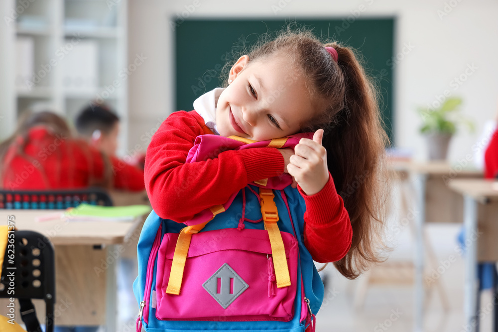 Cute little schoolgirl with backpack in classroom